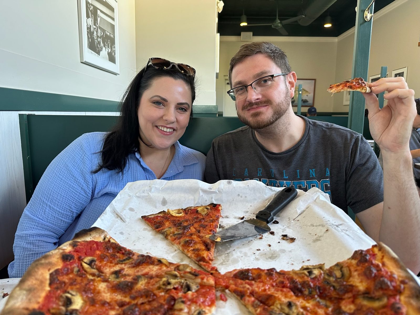 Erin and Andrew in a booth at Frank Pepe's with a mushroom and sausage pizza between them, Andrew holding up a slice.